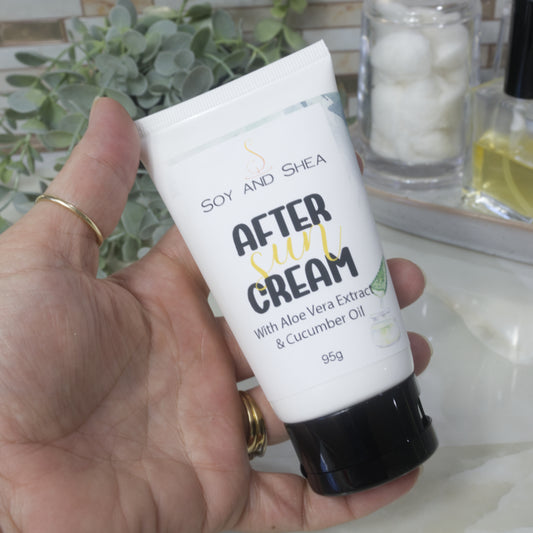 A hand holds a white tube with black flip top cap. In the background is a marble bathroom countertop surrounded by greenery, a jar of cotton balls and bottle of perfume. The tube is labelled as After Sun Cream