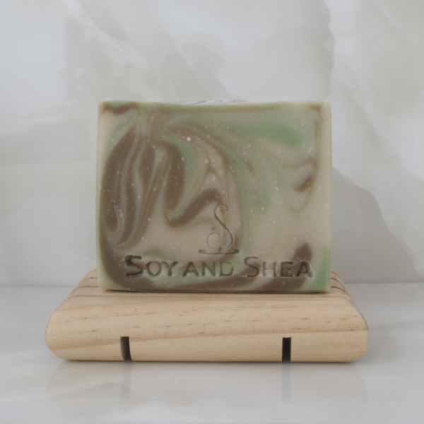 A soap with a light green colour and brown and bright green swirls stands upright on a wooden soap dish surrounded by marble tiles
