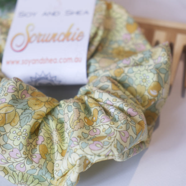 A close up of the fabric design on the Brambles Scrunchie which is a pale yellow fabric covered in bramble like flowers and berries in a varying shades of yellow with mint coloured leaves.