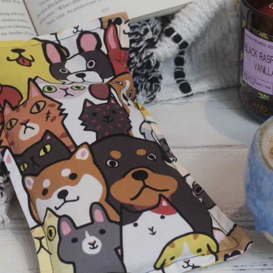 A close up of the Cats and Dogs Mini Heat Pack by Soy and Shea showing the fabric design in more detail. It features hand drawn cats and dogs sitting side by side in rows. Each is drawn in black and filled with bold colours ranging from red and yellow to shades of brown.