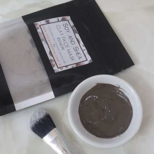 Packet of Soy and Shea Renew Clay Face Mask next to bowl with hydrated powder and a make up brush