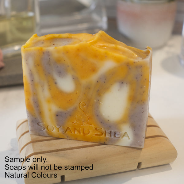 A soap with drops of purple, yellow and white colour sits on a wooden soap dish with a blurred background