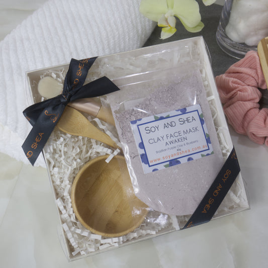 Soy and Shea clay face mask gift box with a clear bag of pale purple powder along with spoon and bowl all tied with dark grey ribbon