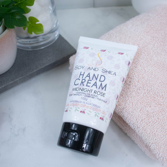 A white tubel with black lids lays across a white marble counter with the top resting on a pink towel. The label features a soft design of scattered roses