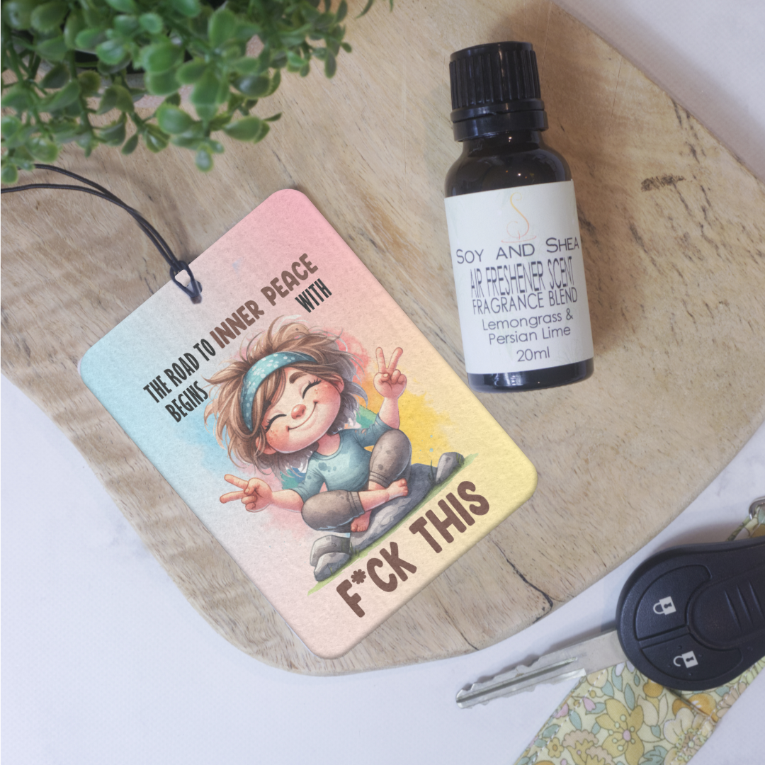 A wooden tray displays the Soy and Shea Inner Peace Car Air Freshener, a bottle of fragrance oil, a potted plant, and car keys with a floral keychain.