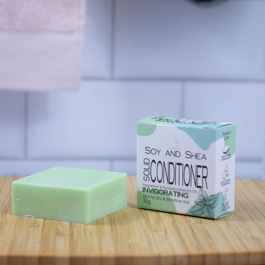 On a wooden tray sits a green bar of conditioner next to a white box with a green abstract pattern reading SOLID CONDITIONER against a blurred tiled background.