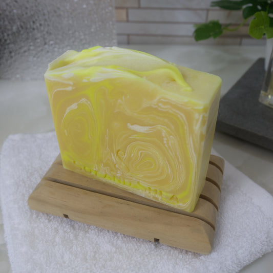 Yellow soap bar with white swirls on a wooden soap dish, placed on a white towel.