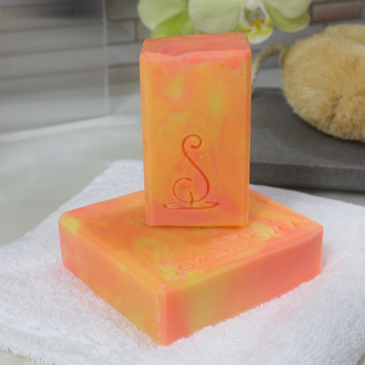 Two soap bars with various shades of orange swirls on a white towel with a blurred background