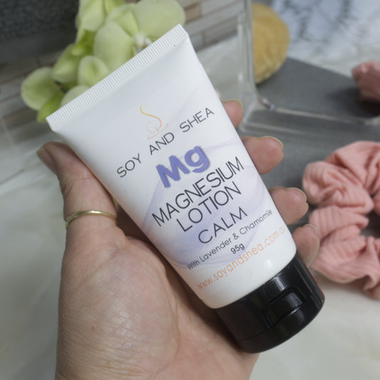 Hand holding a white tube of Soy and Shea Mg Magnesium Lotion Calm with a blurred background