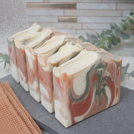Marbled soap bars on a gray surface with a blurred background. The soaps are lined up one in front of the other. Only the front soap shows a marble design of orange, red, white and green