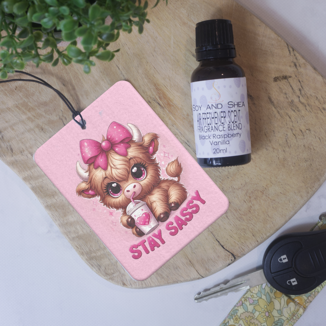 A car air freshener featuring an illustration of a cow with a pink bow and the phrase 'STAY SASSY' on a pink background.