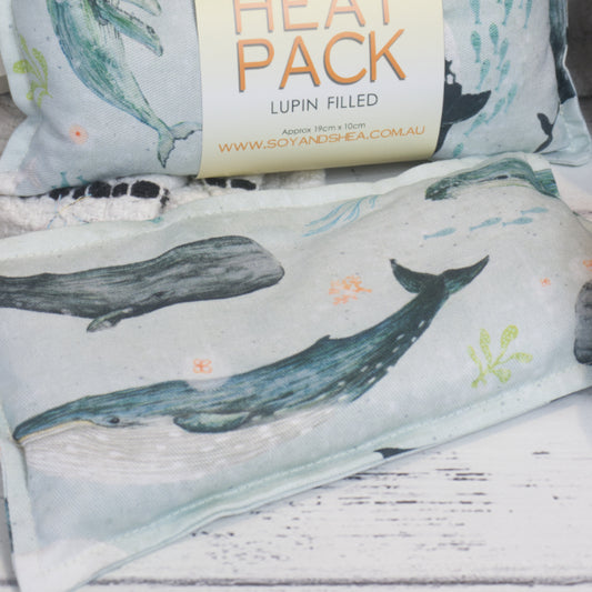 A Whales Mini Heat Pack rests on white side with another packaged Mini Heat Pack behind. The image focuses on the design of the fabric which is pale blue with a variety of whale species