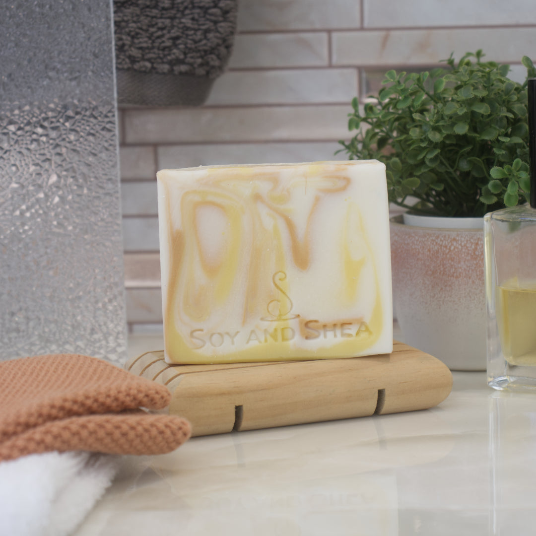 A white soap bar with gold and yellow swirls of colour stands on a wooden stand with a blurred bathroom background