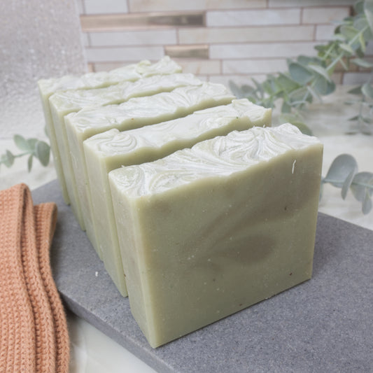 Five pale green soap bars with dark green swirls are lined up one after another on a gray stone surface with a blurred background