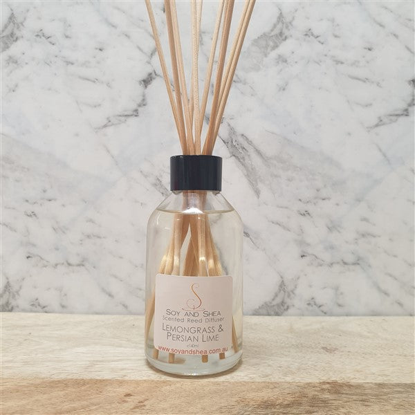 Glass bottle filled with liquid sits on a wooden bench with marble background. The bottle has a bunch of wooden sticks in the top.