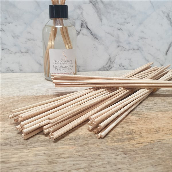A bundle of beige reed diffuser sticks laid out on a wooden surface with a diffuser bottle in the background.