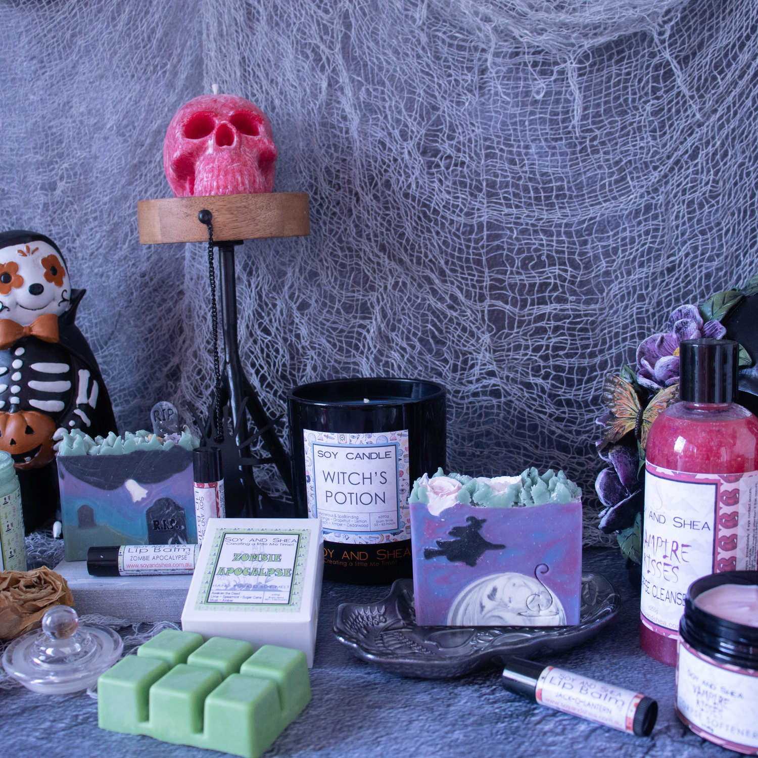A collection of Halloween items sit on a marble bench.  A Red Skull candle sits on a candle stand and below are candles, melts, soaps and moisturiser.