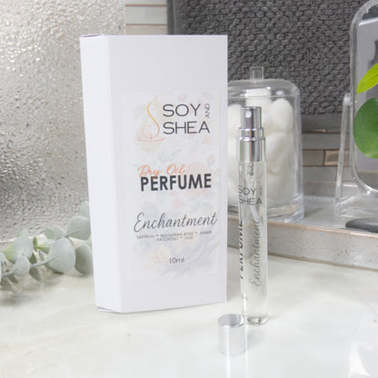 A tall, narrow, clear perfume bottle with a silver atomonise stands upright on a bathroom counter top next to it's packaging and the silver cap.   The packaging is a white box labelled as Dry Oil Perfume Enchantment