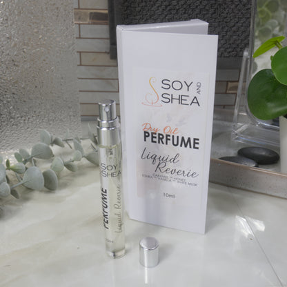 A tall, narrow, clear perfume bottle with a silver atomiser stands upright on a bathroom counter top next to it's packaging and a silver cap.   The packaging is a white box labelled as Dry Oil Perfume Liquid Reverie