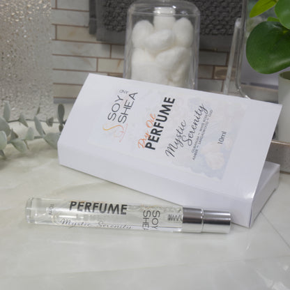 A clear glass perfume atomizer spray bottle with a silver cap lies in front of its white rectangular box. The packaging and bottle are printed with the text 'SOY  and SHEA Dry Oil Perfume Mystic Serenity 10ml'.