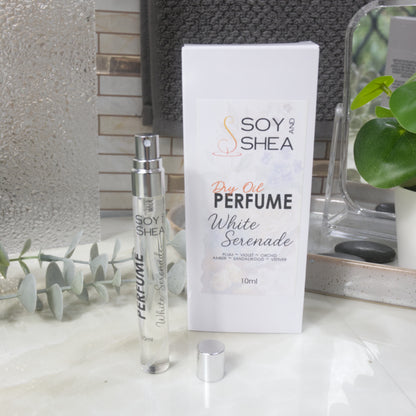 A tall, narrow, clear perfume bottle with a silver atomiser stands upright on a bathroom counter top next to it's packaging and a silver cap.   The packaging is a white box labelled as Dry Oil Perfume Liquid Reverie