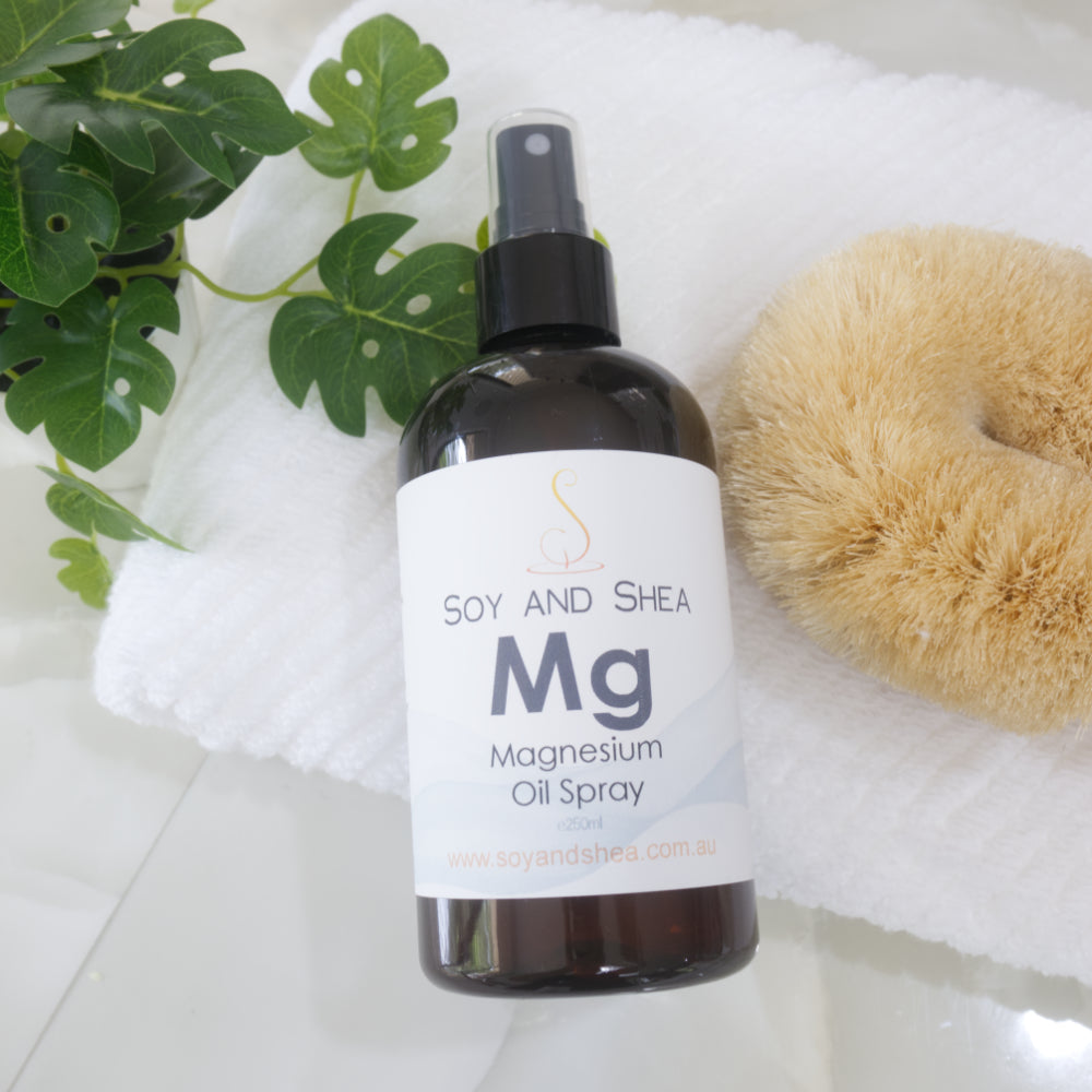 Bottle of Soy and Shea Magnesium Oil Spray resting on a white towel with a plant and sponge in the background