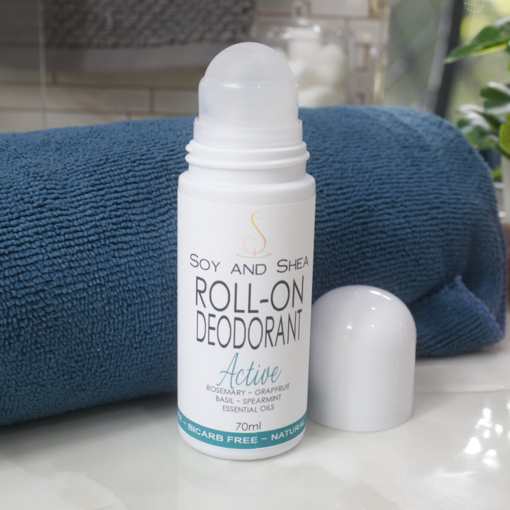 A white bottle with deocrative product label stands on a bathroom counter top in front of a rolled up towel.  The domed lid of the bottle has been removed and placed to the right revealing a ball mechanism