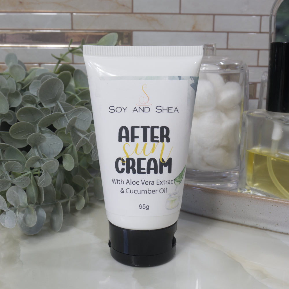 A white tube with black flip top cap sits on a marble bathroom countertop surrounded by greenery, a jar of cotton balls and bottle of perfume.  The tube is labelled as After Sun Cream