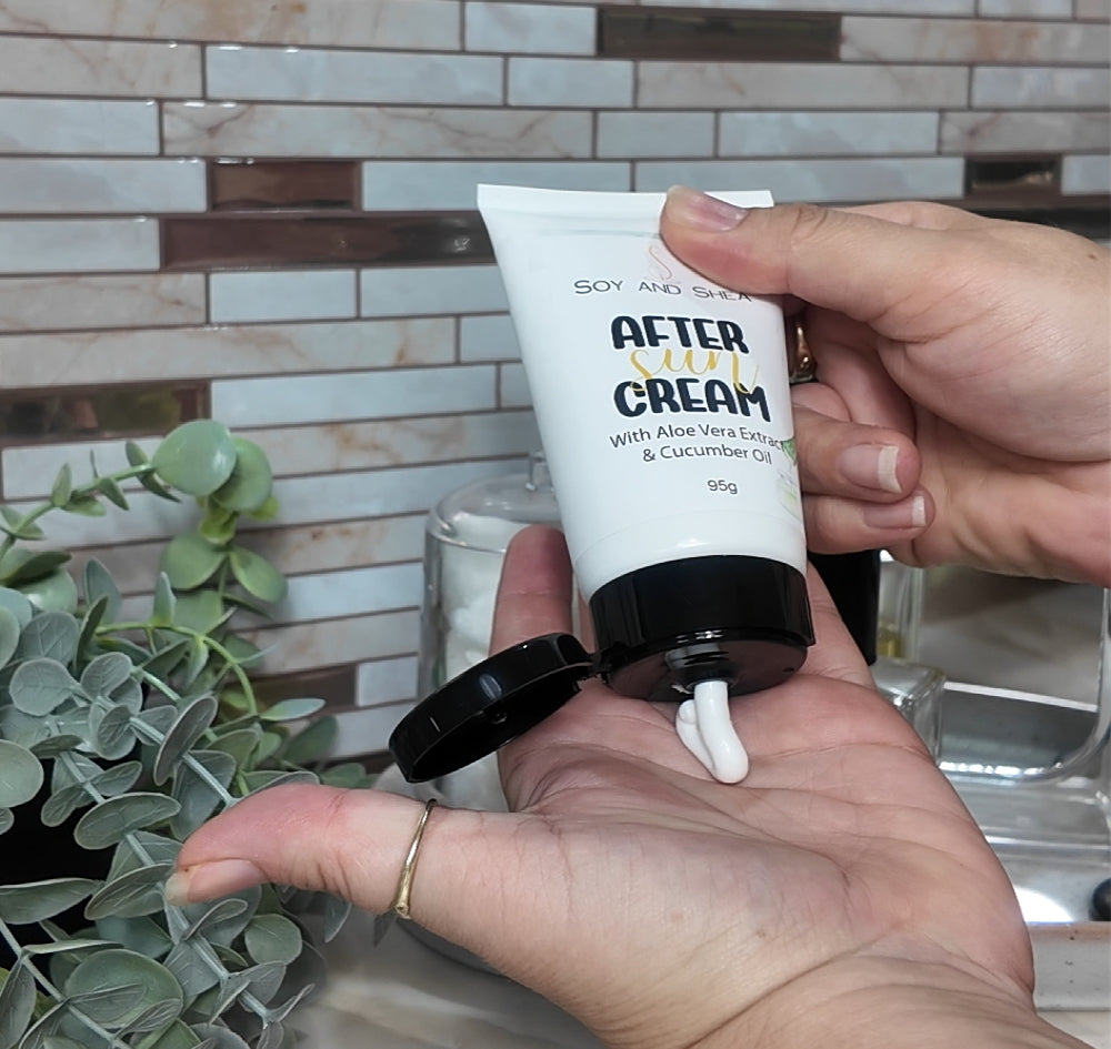 A hand holds a white tube with an open black flip top cap and is squeezing a white cream into the palm of another hand.  In the background is decorative tiled wall and greenery.  The tube is labelled as After Sun Cream