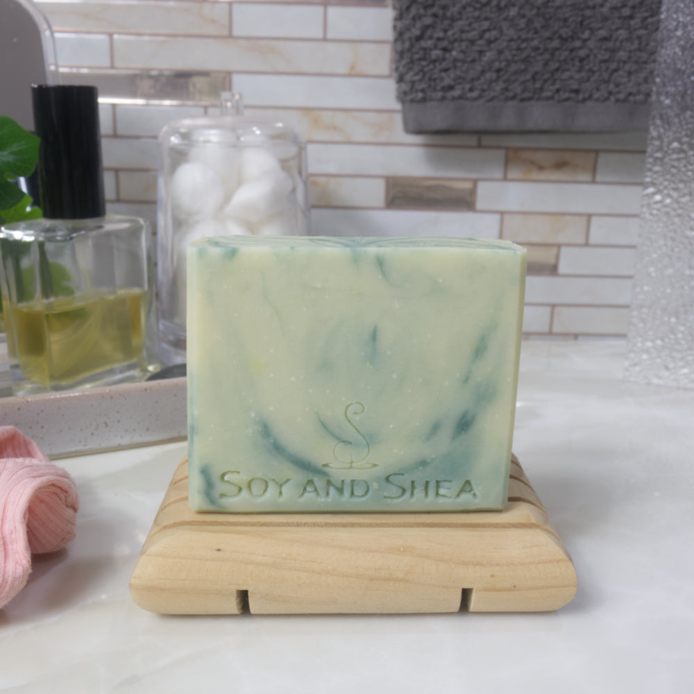 A rectangular bar of soap stands upright on a wooden soap rack on a bathroom coutertop.  The soap has a pale green base colour with dark green streaks of colour