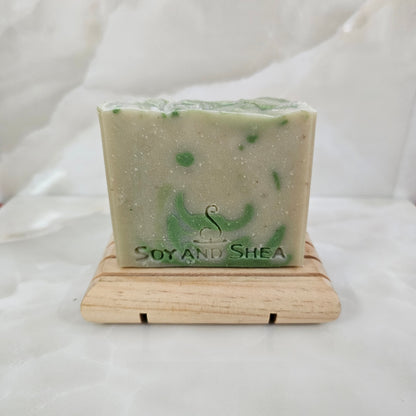 Pale Green Soap bar with dark green drops sits on a wooden soap rack on a white marble background