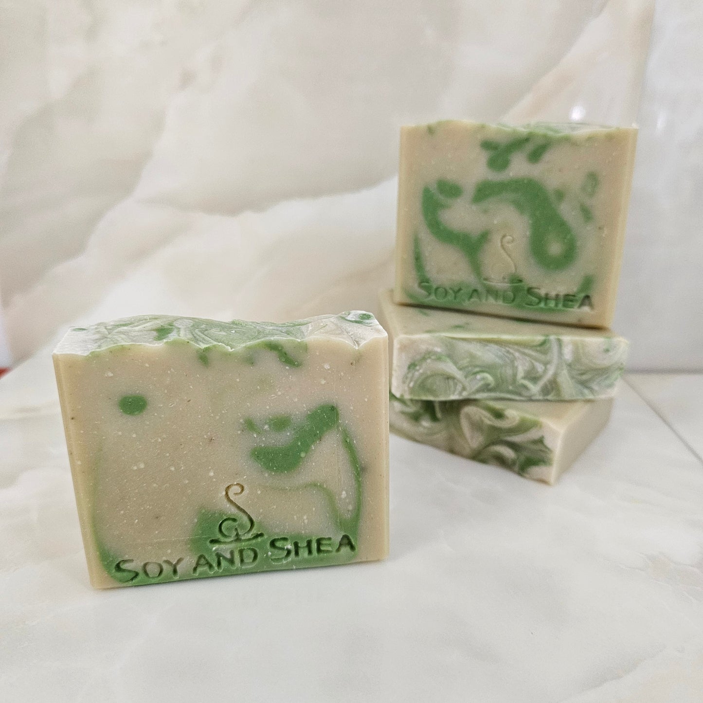 A selection of Pale Green Soap bars with dark green drops sits white marble background.  Each soap shows various designs in the drop
