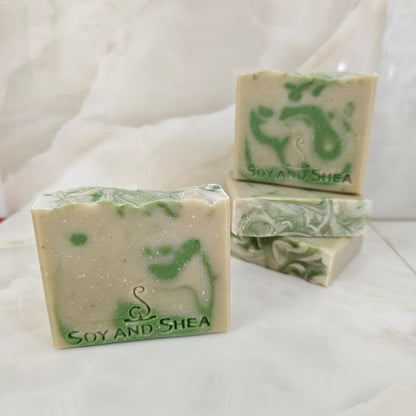 A selection of Pale Green Soap bars with dark green drops sits white marble background.  Each soap shows various designs in the drop