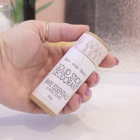 A hand holds a cardboard tube labelled as SOLID STICK DEODORANT against a blurred bathroom background. 
