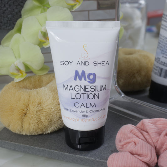 White tube of Soy and Shea Magnesium Lotion on a bathroom counter with flowers and a mirror in the background.