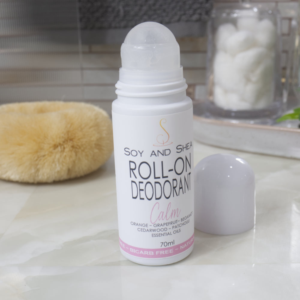 A white bottle with deocrative product label stands on a bathroom counter top along with body brush and accessories.  The domed lid of the bottle has been removed and placed to the right revealing a ball mechanism