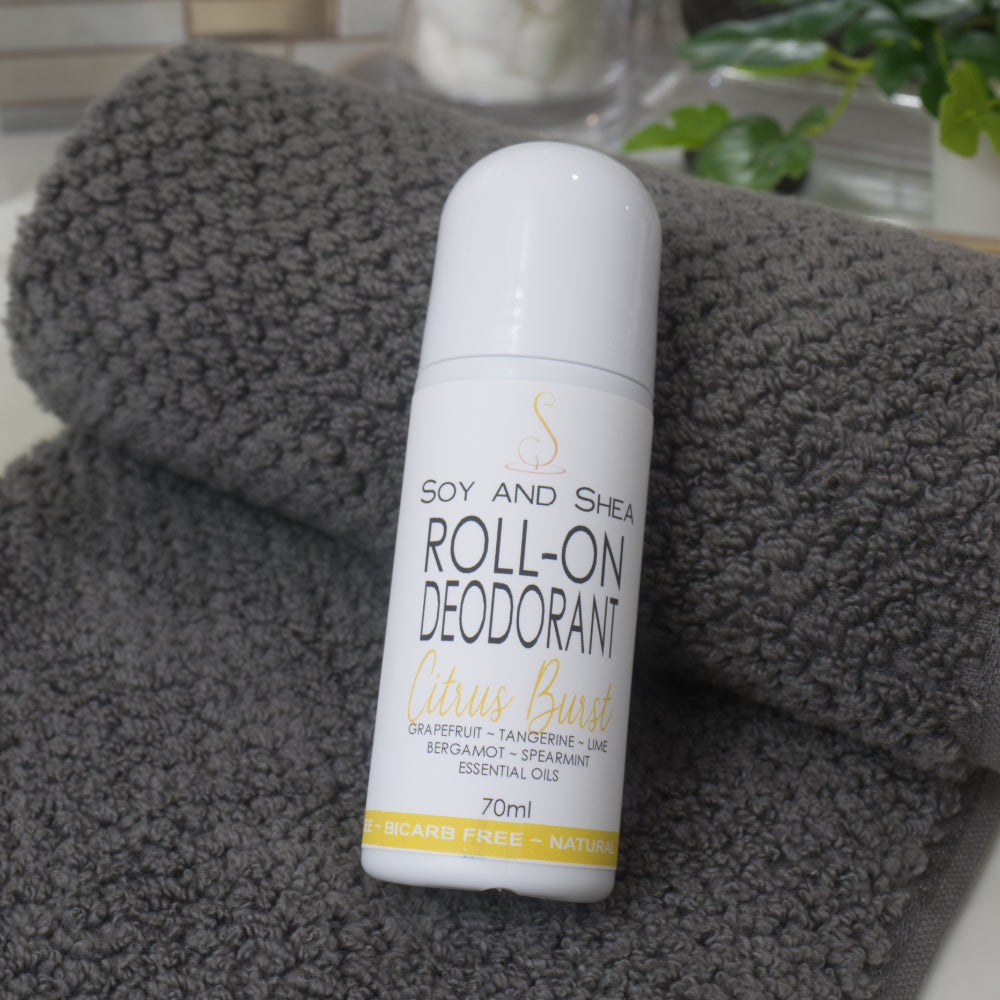A white bottle with domed lid labelled as Roll-On Deodorant lies resting against a grey towel with a blurred background of a bathroom countertop