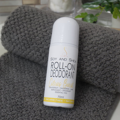 A white bottle with domed lid labelled as Roll-On Deodorant lies resting against a grey towel with a blurred background of a bathroom countertop