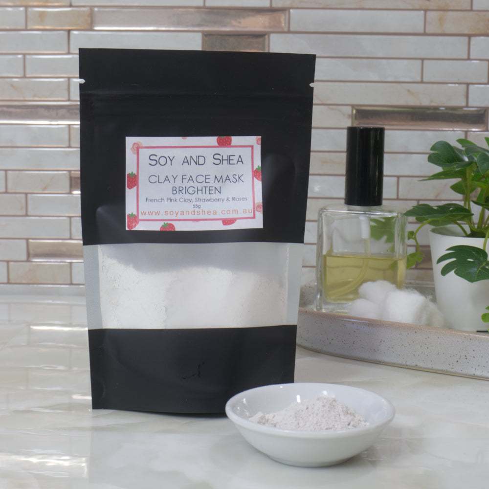 Soy and Shea Brighten Clay Face Mask packaging on a marble surface with a small white bowl in front, filled with pink powder