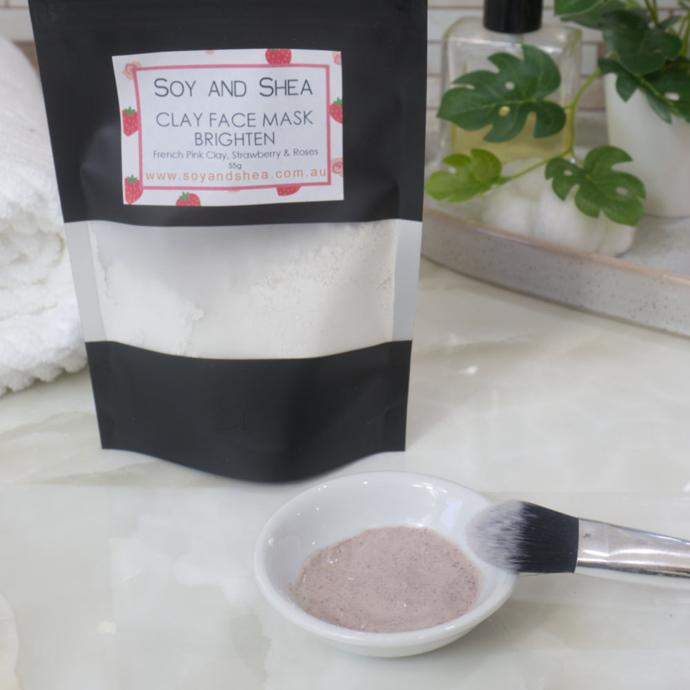 Soy and Shea Clay Face Mask packaging with a small bowl of hydrated mask powder and a brush on a white surface.