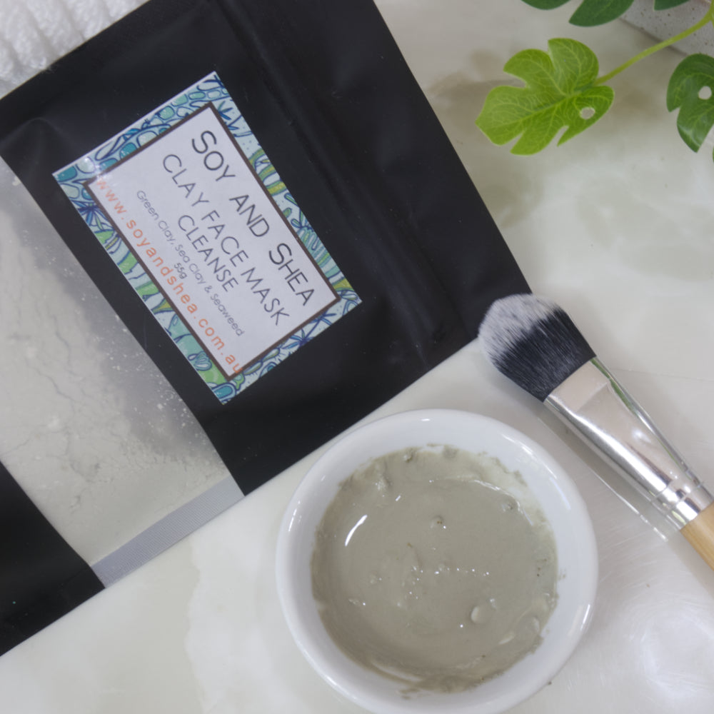 Soy and Shea Cleanse Clay Face Mask packaging with a brush and white bowl filled with wet clay on a white surface