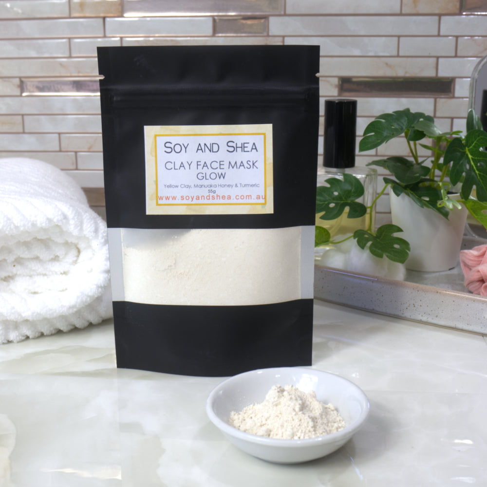 Soy and Shea Glow clay face mask packaging with a bowl of yellow powder on a bathroom counter.