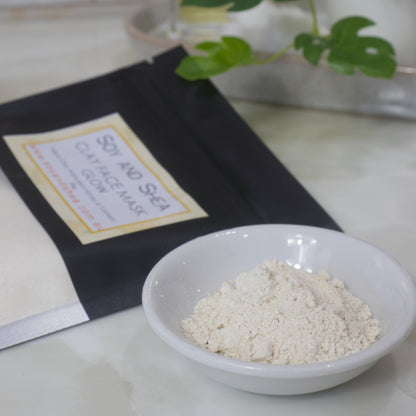 Yellow powder in a bowl with a black bag labeled 'Soy and Sea Clay Mask' on a light surface.