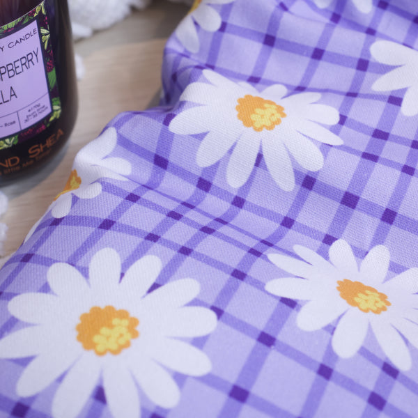 A close up of the a heat pack with a purple checkered pattern and white daisy designs