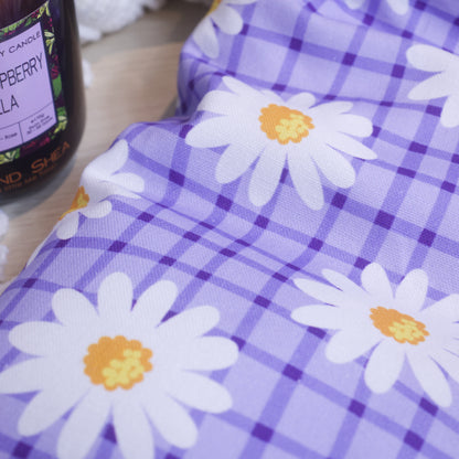 A close up of the a heat pack with a purple checkered pattern and white daisy designs