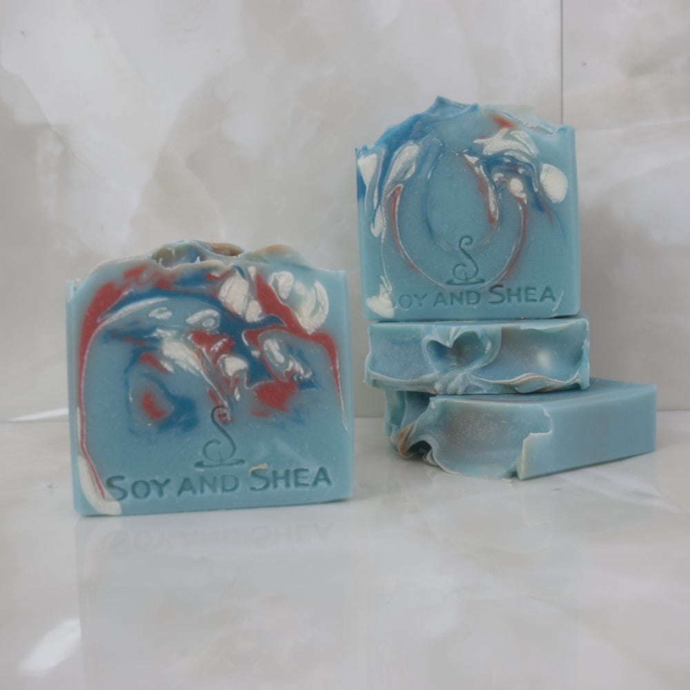 Bars of blue soap with marbled patterns on a white surface, branded 'Soy and Shea'.