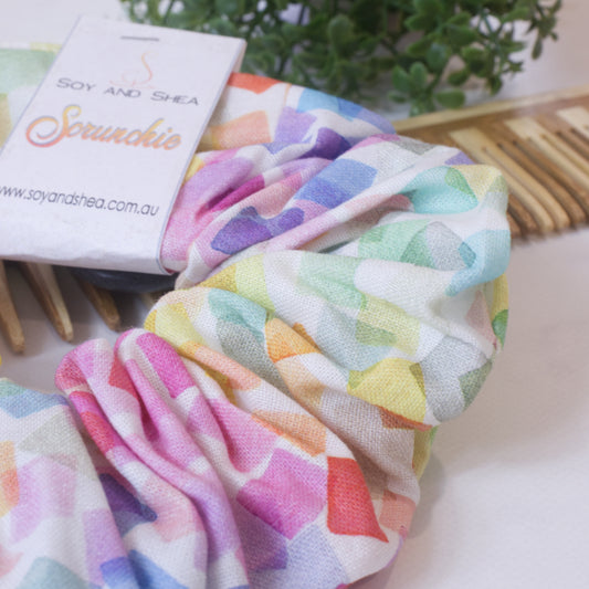 A close up image of the Confetti scrunchie showing lots of squares in various colours of the rainbow with a watercolour look, randomly placed on a white background.