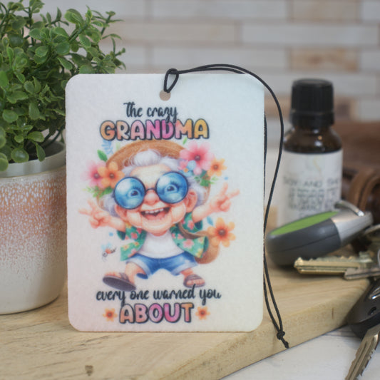A car air freshener featuring an illustration of a hippie-like grandmother with glasses and flowers, and the text 'The crazy GRANDMA everyone warned you ABOUT'. 