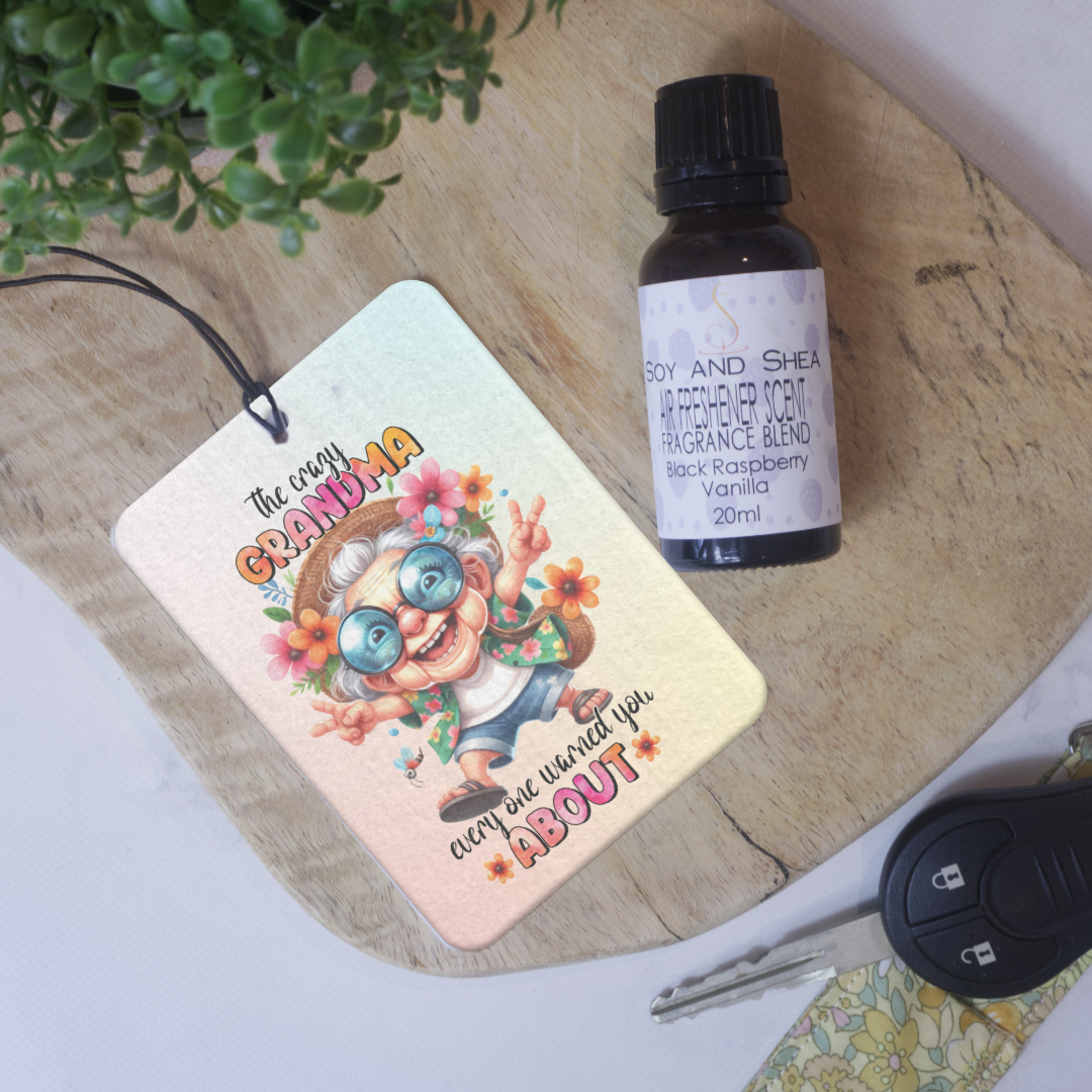 A car air freshener featuring an illustration of a hippie-like grandmother with glasses and flowers, and the text 'The crazy GRANDMA everyone warned you ABOUT' lies on a wooden surface next to a bottle of scent