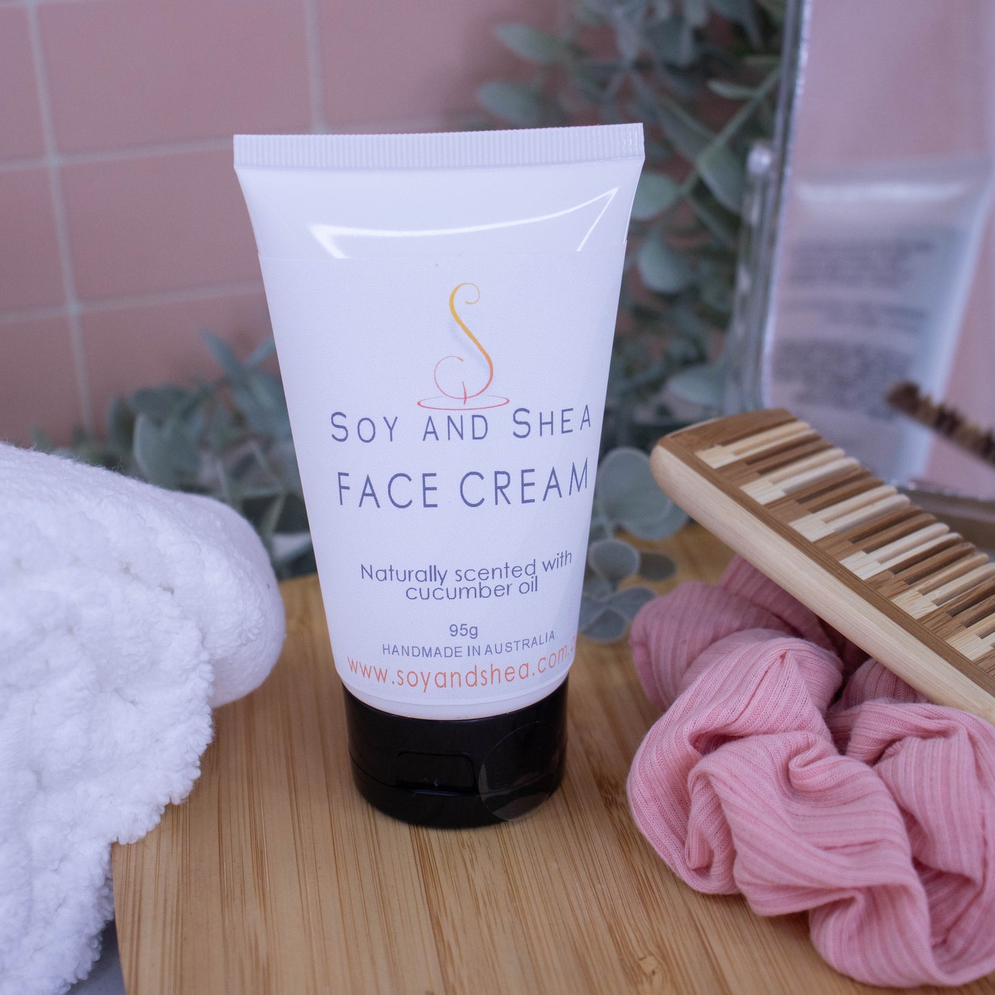 A white tube of Face Cream with black lid sits on a wooden bench surrounded by a white towel, mirror, Comb and scunchie.